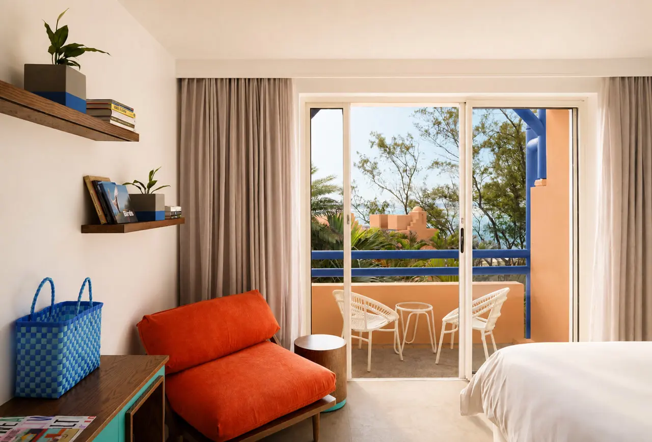 Garden View Room - Contemporary hotel room with a private balcony, colourful lounge chair, and views of tropical gardens.